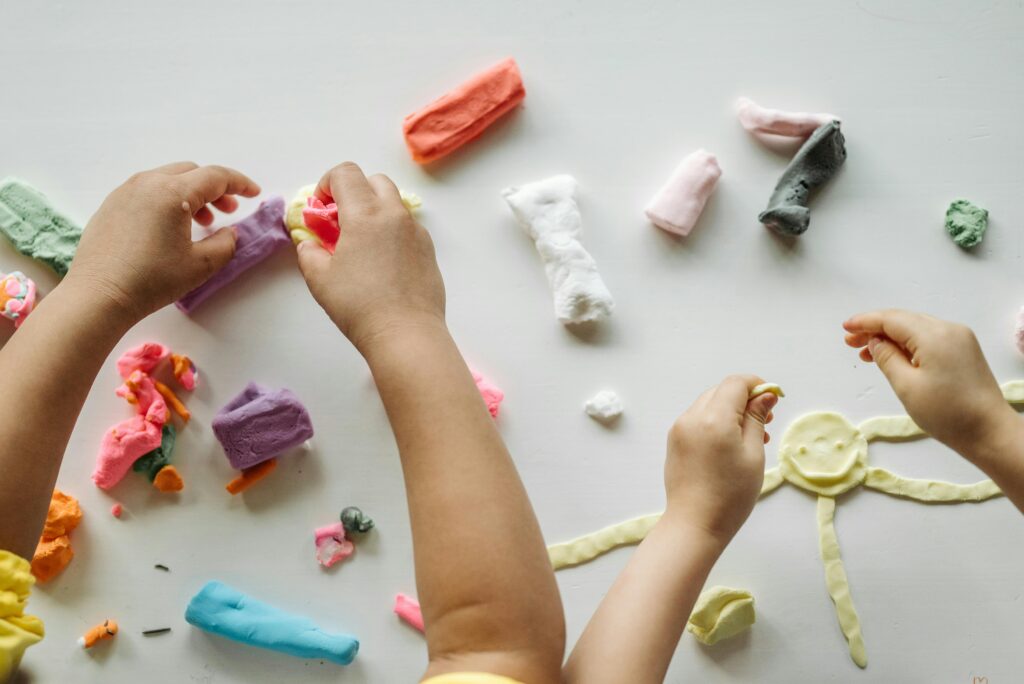 Children engaged in creative clay play, forming shapes and exploring colors on a white table.
